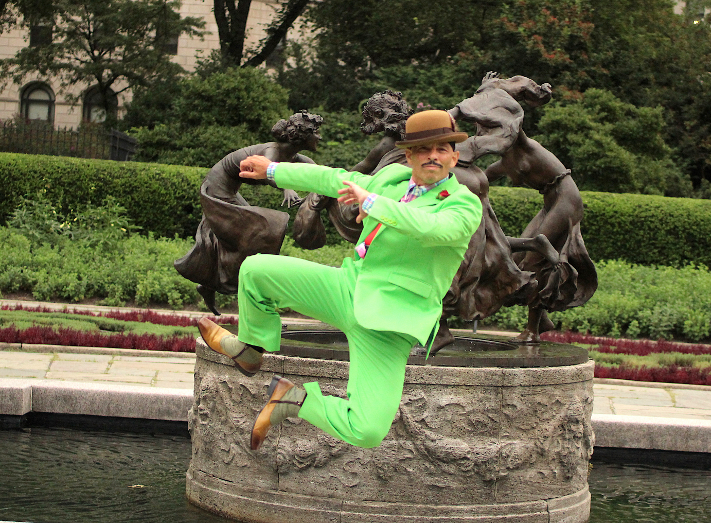 In a bright green suit, Arthur Aviles clicks his heels together. He wears a derby and has a thin mustache.
